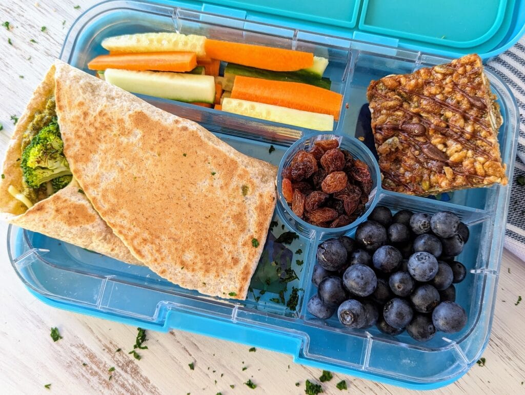 Vegan lunchbox with broccoli pesto pocket, blondie muesli bar, fruit and veggies.